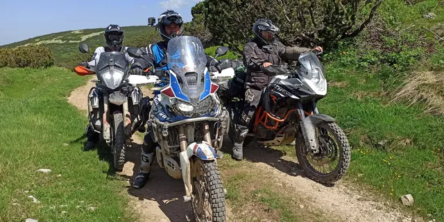 Tři jezdci na enduro motorkách na polní cestě.